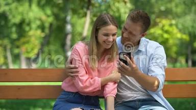 快乐的一对情侣一起在公园里看智能手机上的照片，约会